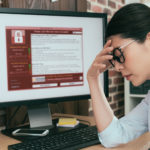 Vrouw die met de handen in de haren zit en merkt dat haar computer gehackt is.