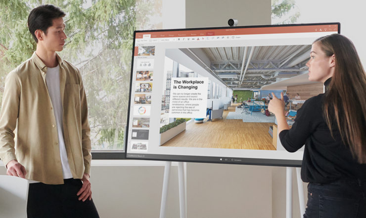 un homme et une femme debout devant un Surface Hub 2S