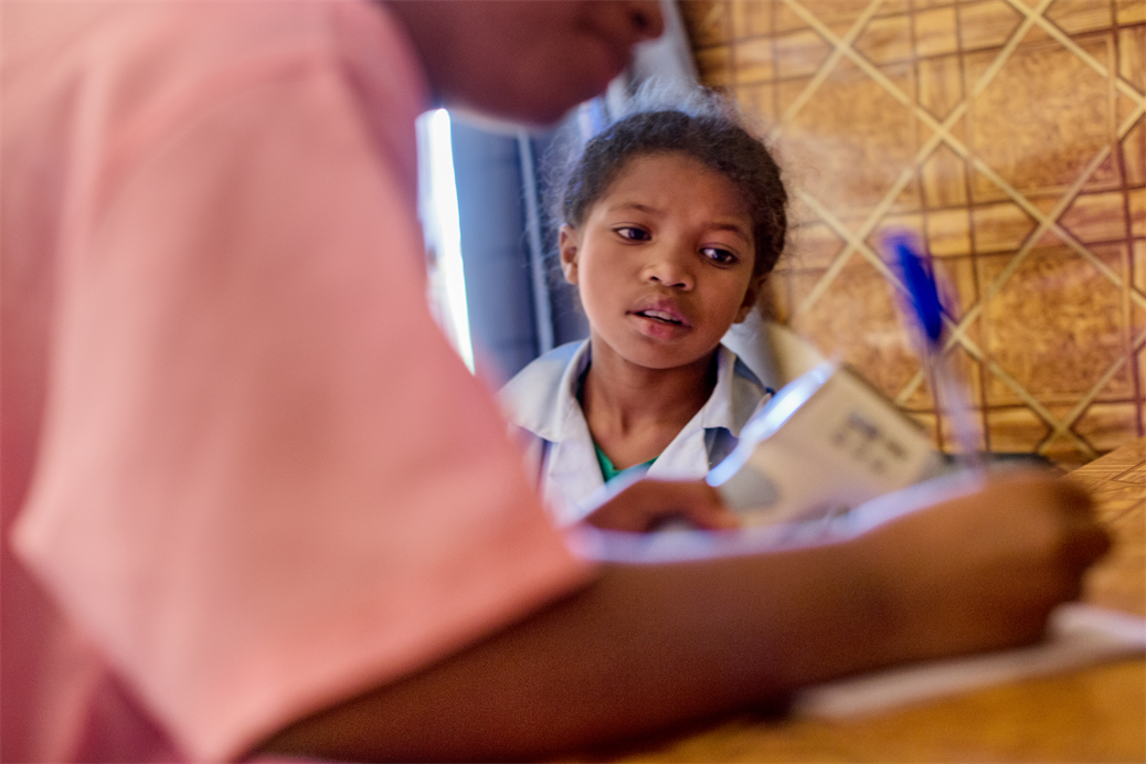 A female child sitting and looking as a nurse writes in notebook in rural clinic of nutrition enhancement program in Madagascar.