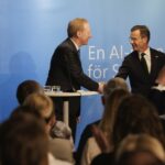 Två personer skakar hand på en scen framför en publik.