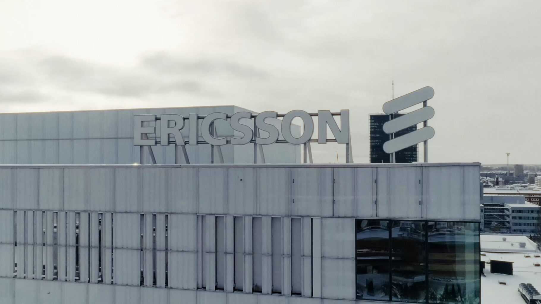 Ericssons logotyp på taket till en stor kontorsbyggnad under en mulen himmel.