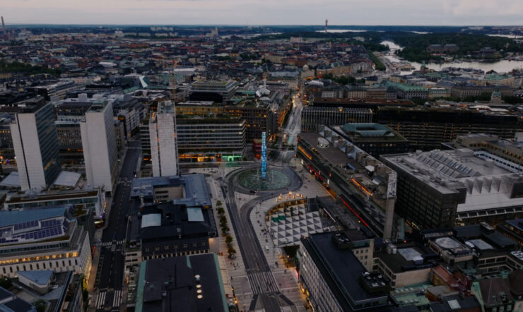 Aerial view of a city center at dusk, with office buildings, streets, a roundabout, and construction areas surrounded by a dense urban landscape.
