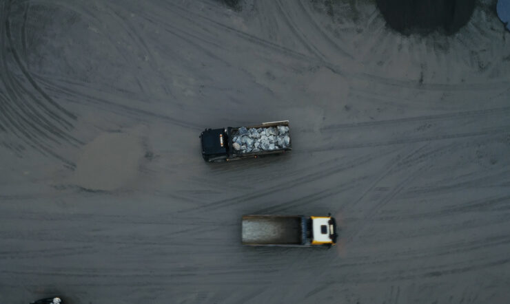 Aerial view from above of two trucks on a large gravel-covered site, one carrying a load of material.