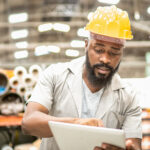 Two workers at a factory, looking at a device