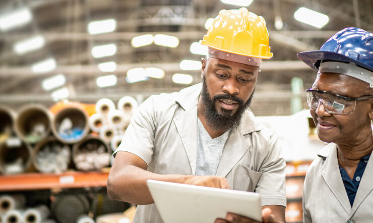 Two workers at a factory, looking at a device